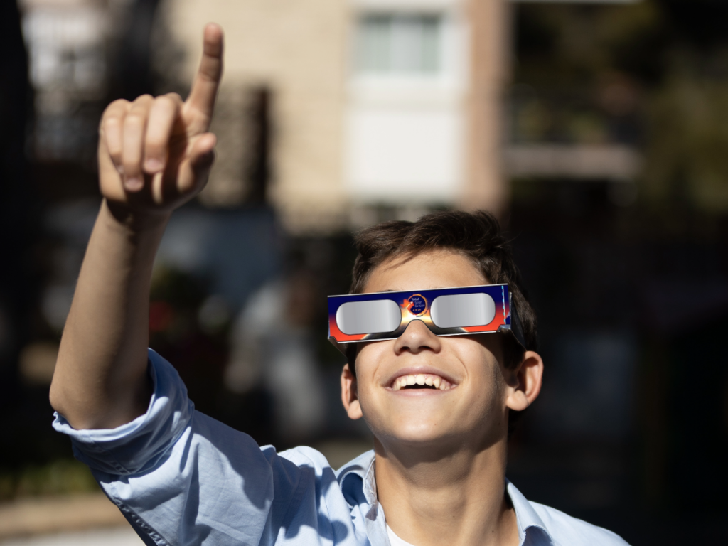 A young boy wearing solar eclipse glasses and pointing upwards.