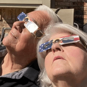 Two adults outside wearing total eclipse glasses