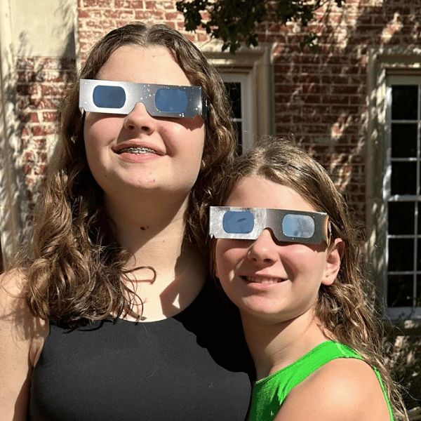 Two girls outside wearing total eclipse glasses