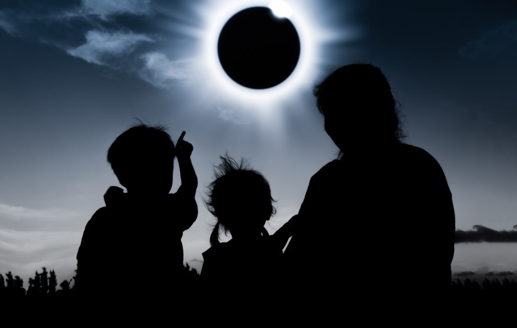 Three people with their backs to the camera watching a Total Solar eclipse