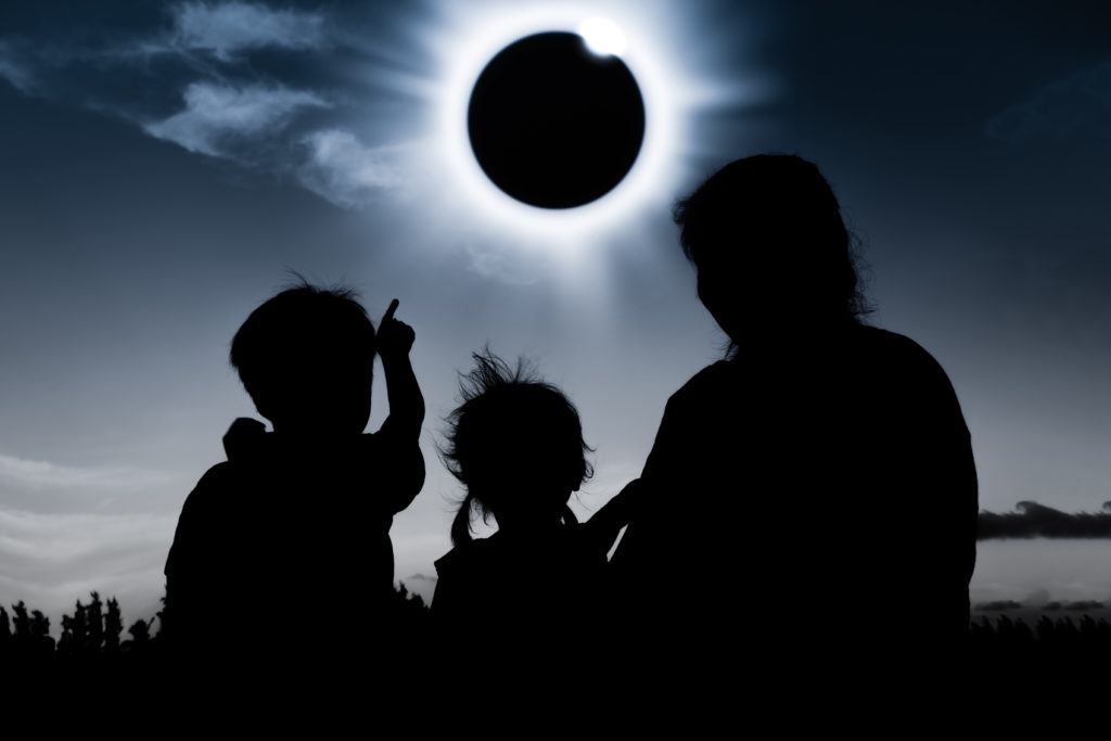 Three people with their backs to the camera watching a Total Solar eclipse