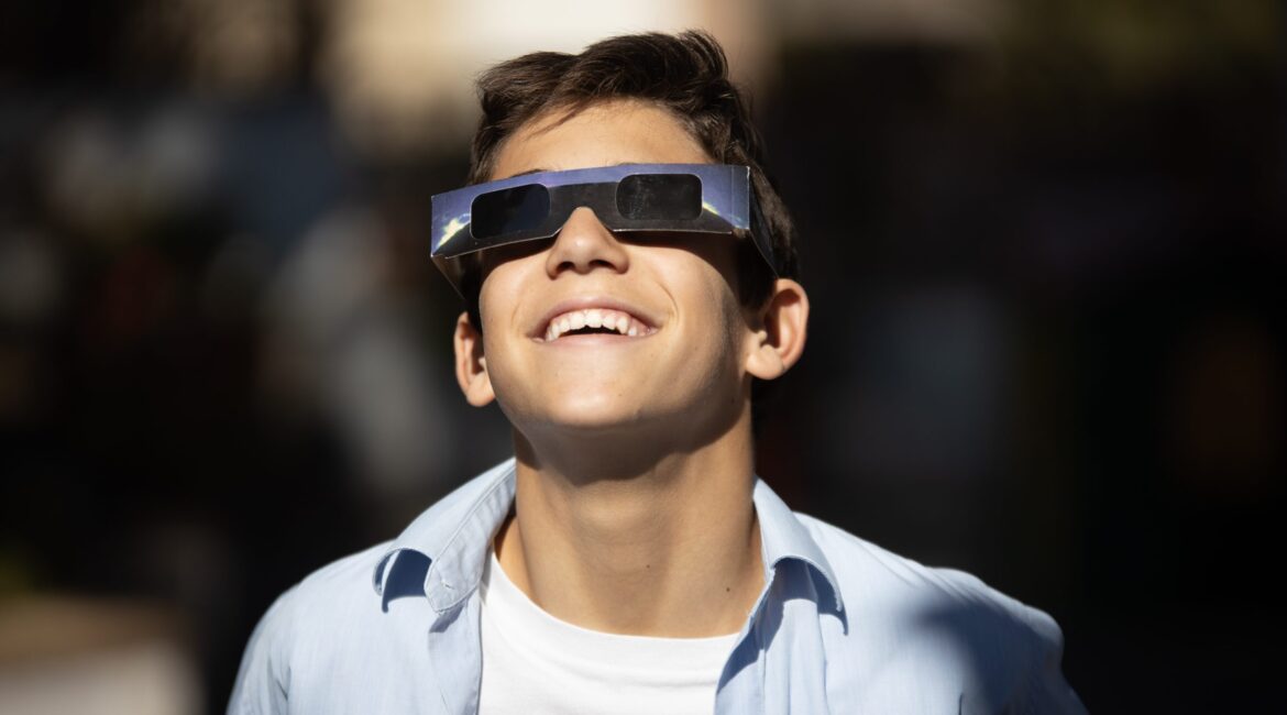 A kid wearing solar eclipse glasses looking up